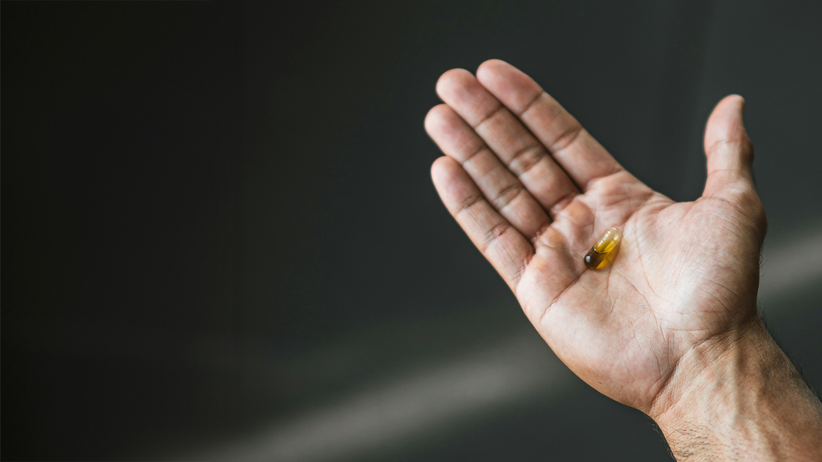 Open palm holding a single golden supplement capsule against a dark background